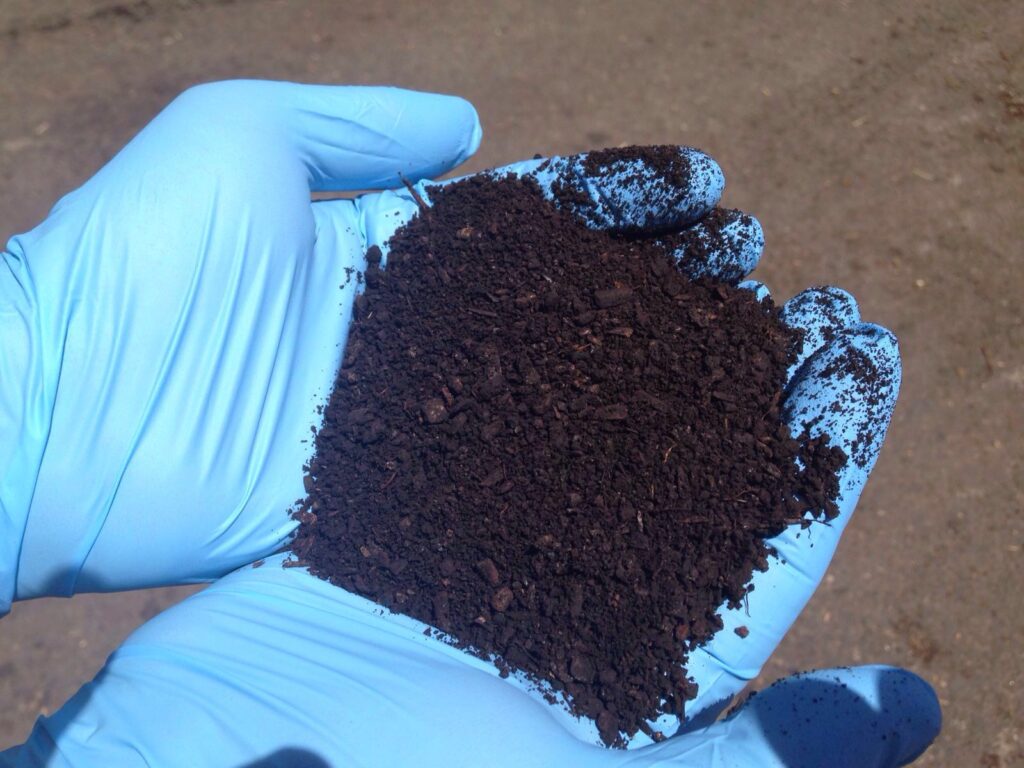 Mani guantate mostrano un campione di terriccio scuro.